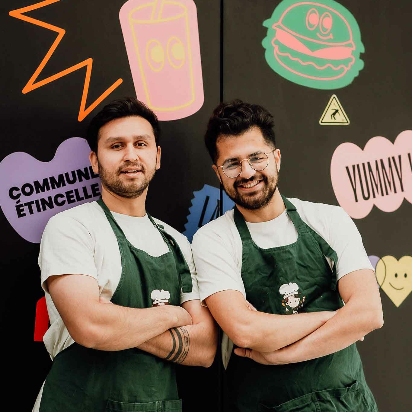 Les deux chefs du restaurant posent devant des illustrations colorées à La Commune, symbolisant leur créativité culinaire.