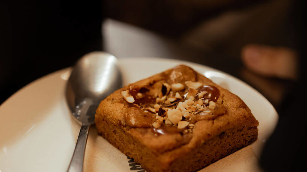 Délicieux brownie garni de caramel et d'éclats de noisettes, servi sur une assiette blanche avec une cuillère au restaurant de La Commune à Lyon.