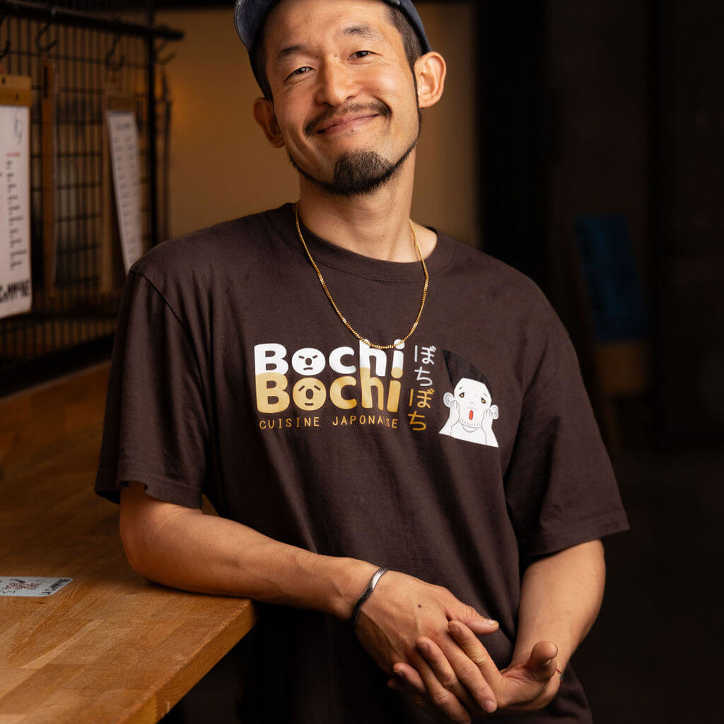 Portrait d'un chef japonais souriant, vêtu d'un t-shirt Bochi Bochi, spécialiste de cuisine japonaise à La Commune.