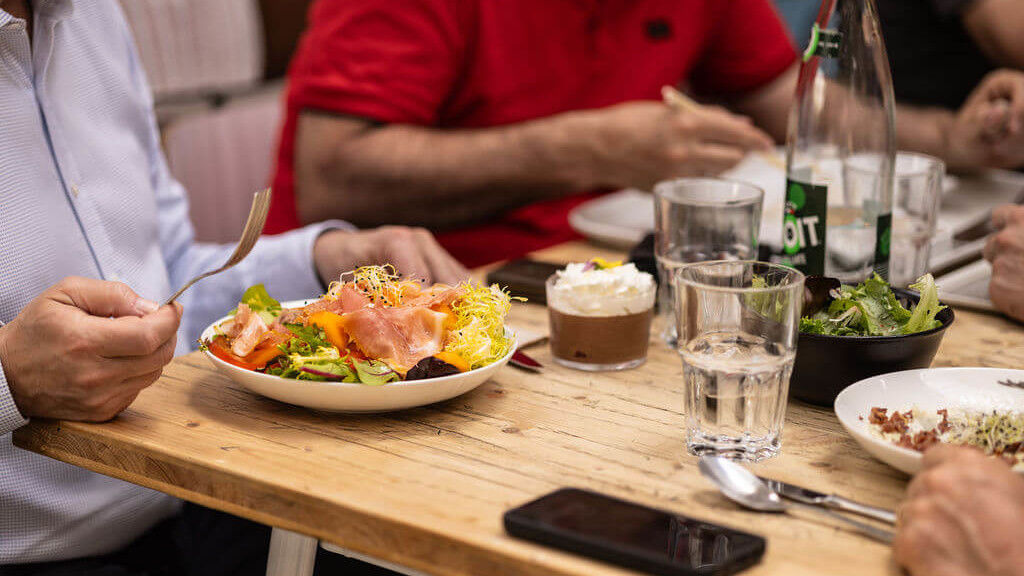 Repas convivial autour d’une salade garnie de saumon et légumes, accompagné de boissons et d’un dessert, partagés sur une table en bois.