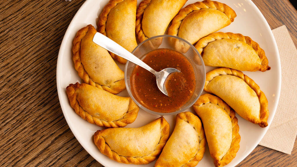 Assiette de délicieux empanadas dorés, accompagnés d'une sauce salsa épicée, servie sur une table en bois au restaurant de La Commune, Lyon.