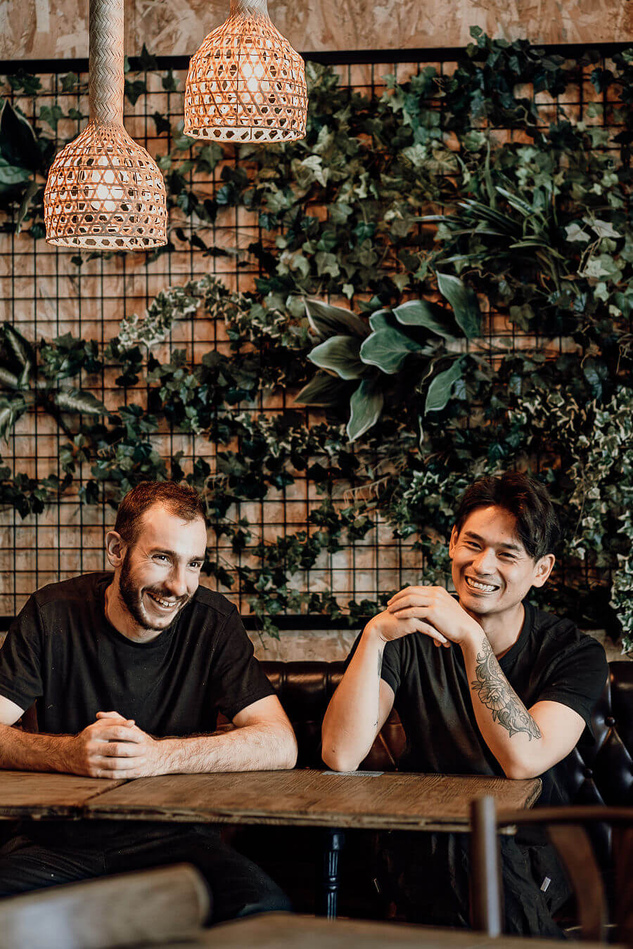 Deux chefs souriants posent devant un mur végétal, ambiance conviviale et détendue.