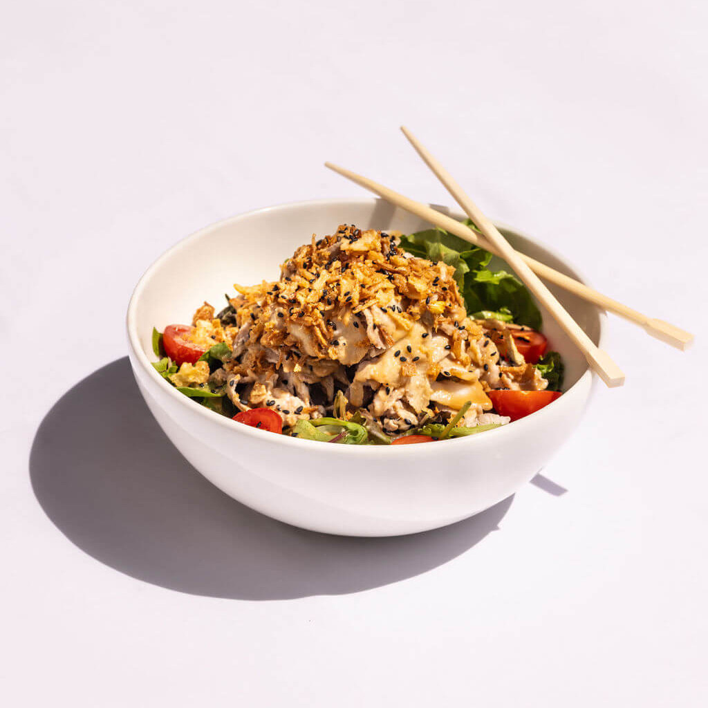 Bol de salade asiatique garnie de poulet et d’oignons frits, présenté avec des baguettes, offrant un repas sain et savoureux.