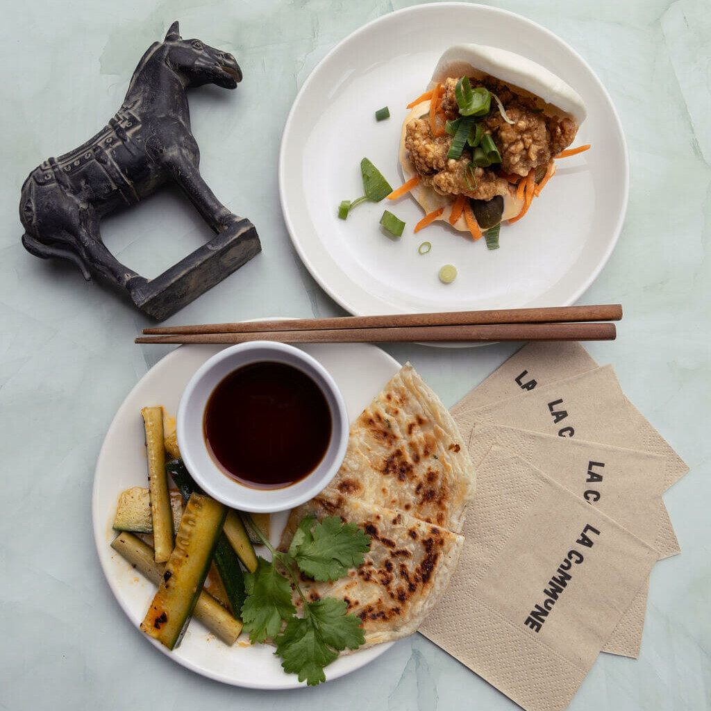 Assiette combinée comprenant un bao au poulet frit, une galette de Shanghai, des légumes marinés et une sauce, accompagnée d'une figurine de cheval noir