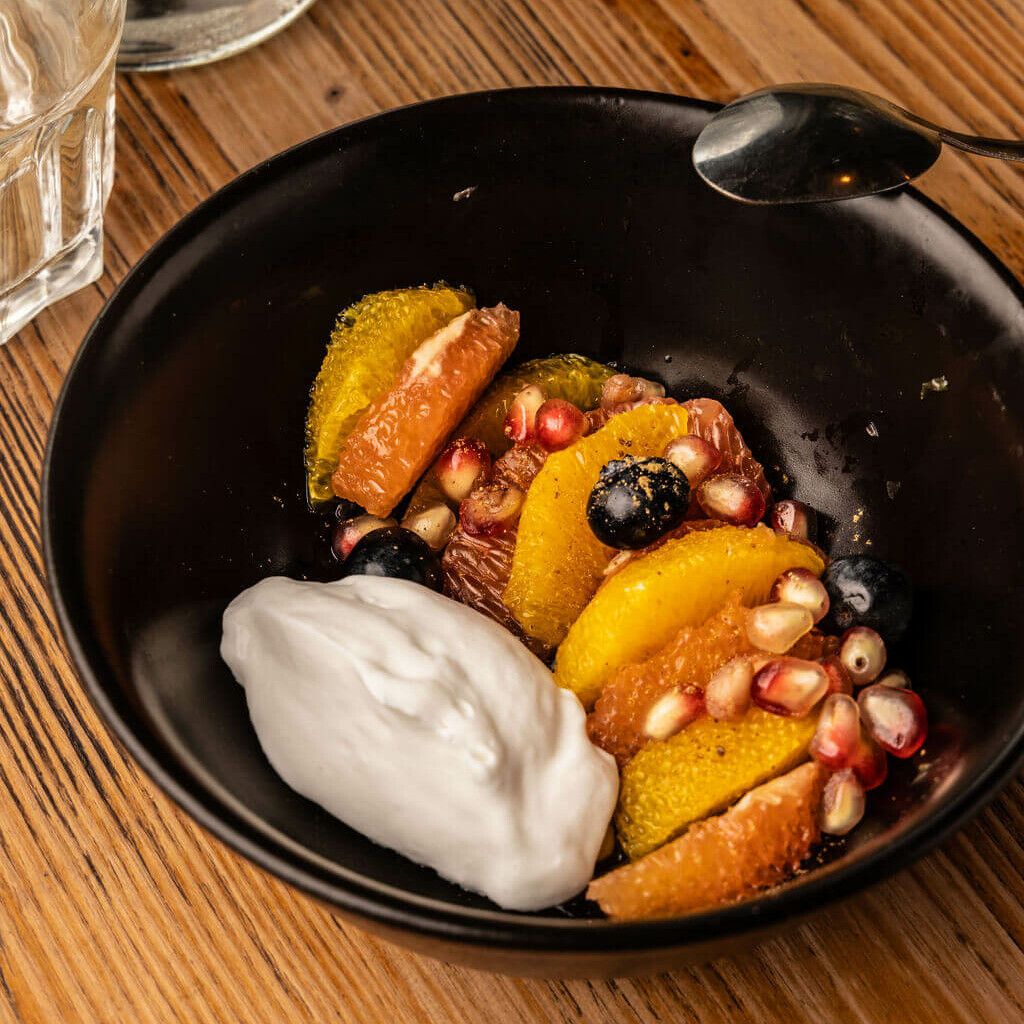 Dessert fruité aux agrumes, grenade, myrtilles et chantilly coco dans un bol noir